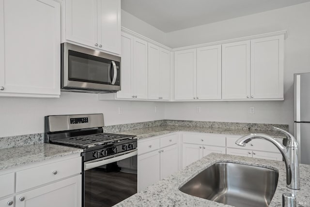 kitchen with appliances with stainless steel finishes, a sink, white cabinetry, and light stone countertops