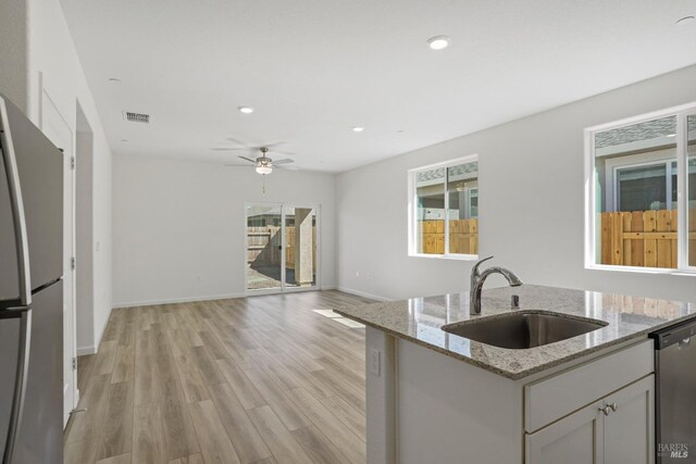 kitchen featuring sink, ceiling fan, light stone countertops, appliances with stainless steel finishes, and light hardwood / wood-style floors