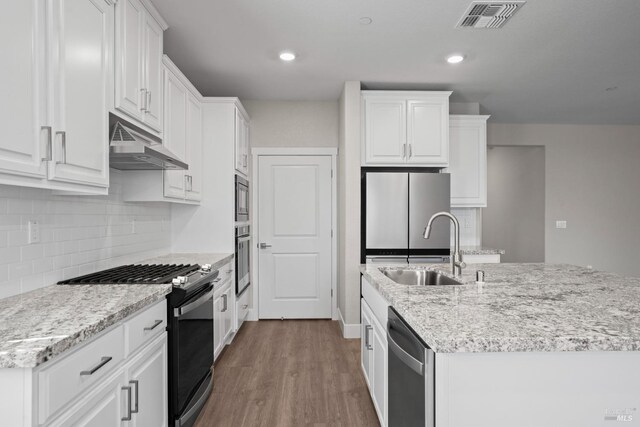 kitchen with visible vents, a kitchen island with sink, under cabinet range hood, a sink, and appliances with stainless steel finishes