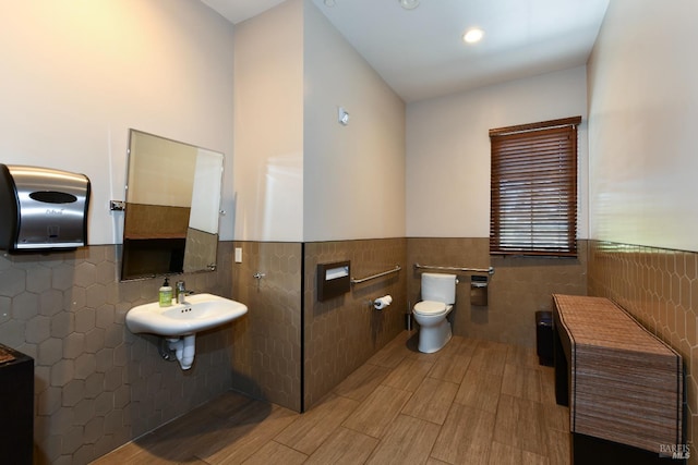 half bathroom featuring wainscoting, a sink, toilet, and tile walls