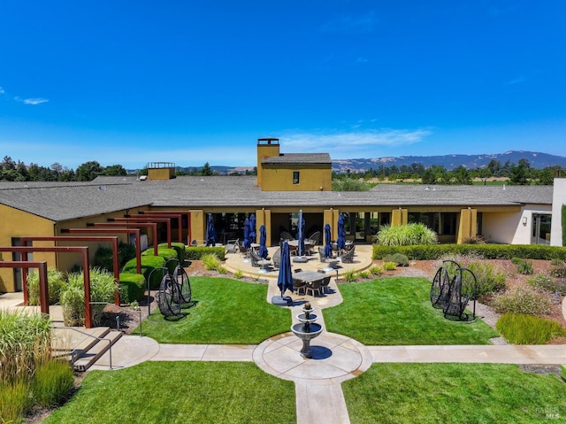 rear view of house with a mountain view, stucco siding, a yard, and a patio