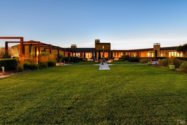 back of house at dusk with a lawn and a chimney