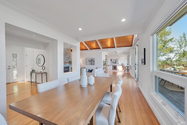 dining space with crown molding, light hardwood / wood-style flooring, a stone fireplace, and wooden ceiling