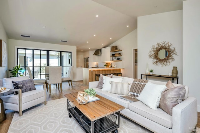 living area featuring high vaulted ceiling, light wood-type flooring, visible vents, and recessed lighting