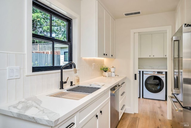 clothes washing area featuring washer / clothes dryer, cabinet space, visible vents, light wood-style floors, and a sink