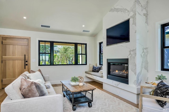 living room with lofted ceiling, light wood finished floors, a high end fireplace, and visible vents