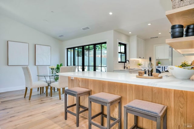 kitchen featuring a peninsula, a sink, visible vents, white cabinets, and open shelves