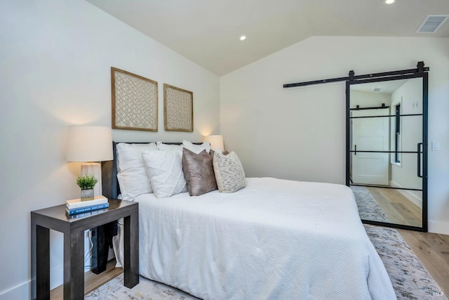 bedroom featuring lofted ceiling, recessed lighting, visible vents, light wood-style flooring, and a barn door