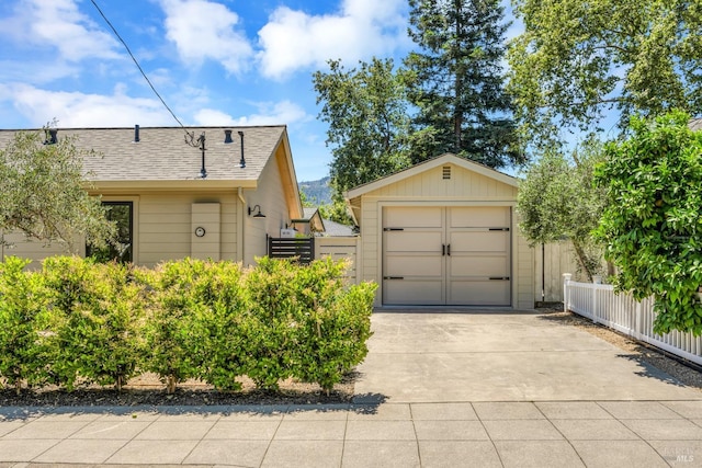 exterior space featuring roof with shingles, fence, concrete driveway, and an outdoor structure