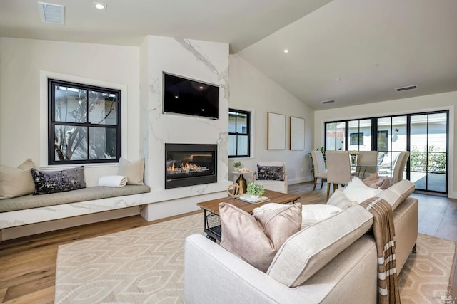 living area featuring a high end fireplace, visible vents, vaulted ceiling, and light wood finished floors