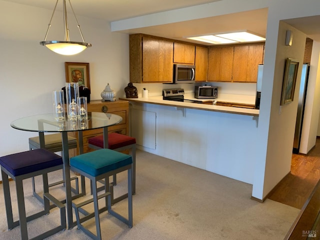 kitchen featuring stainless steel appliances, a peninsula, light countertops, brown cabinets, and decorative light fixtures