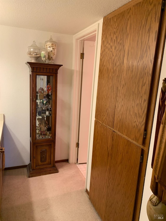 corridor with a textured ceiling, light carpet, and baseboards