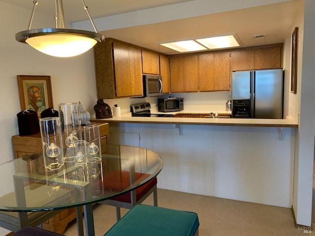 kitchen with brown cabinetry, light colored carpet, appliances with stainless steel finishes, a peninsula, and light countertops