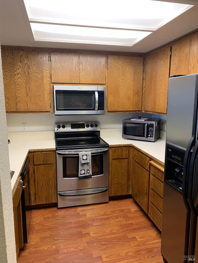 kitchen featuring light countertops, appliances with stainless steel finishes, brown cabinetry, and light wood-style flooring