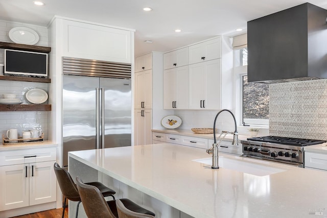 kitchen with ventilation hood, backsplash, white cabinetry, and a kitchen breakfast bar