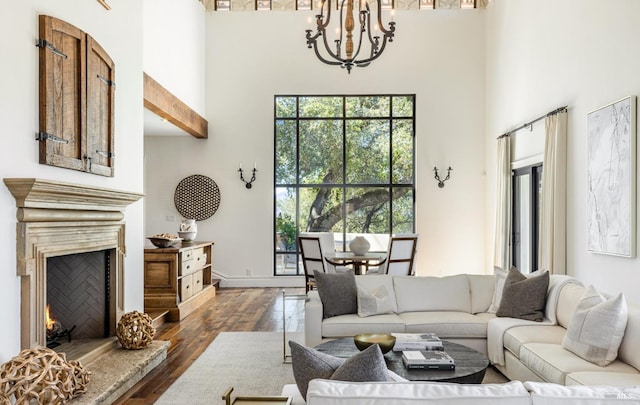 living area with a chandelier, a warm lit fireplace, a high ceiling, and dark wood-style flooring