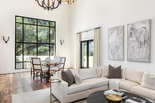 living room featuring wood-type flooring, a high ceiling, baseboards, and an inviting chandelier