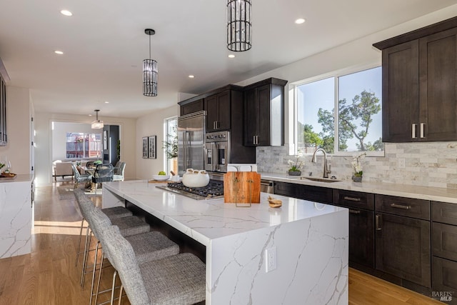 kitchen with sink, appliances with stainless steel finishes, a center island, light stone countertops, and decorative light fixtures