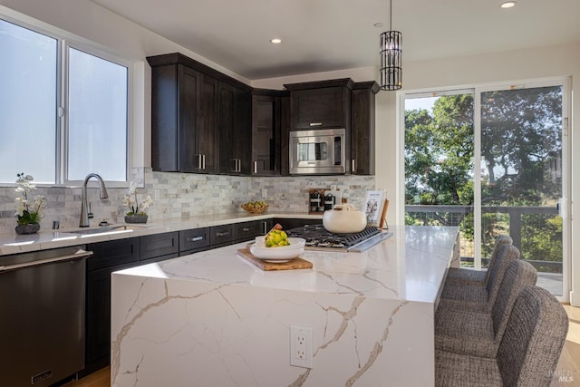 kitchen with decorative light fixtures, tasteful backsplash, sink, stainless steel appliances, and light stone countertops