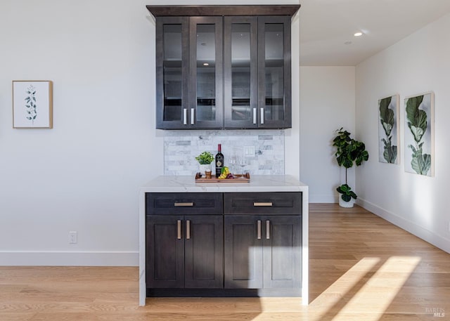 bar featuring tasteful backsplash, light stone countertops, light wood-type flooring, and dark brown cabinetry