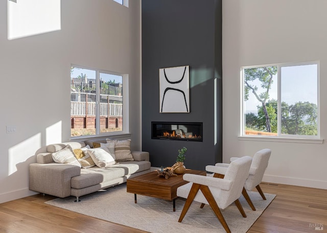 living room with a towering ceiling, a large fireplace, and light wood-type flooring