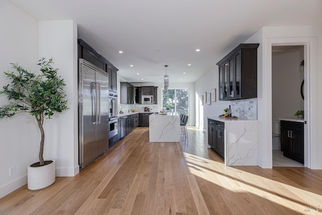 kitchen with light stone counters, built in appliances, decorative light fixtures, light wood-type flooring, and a kitchen island