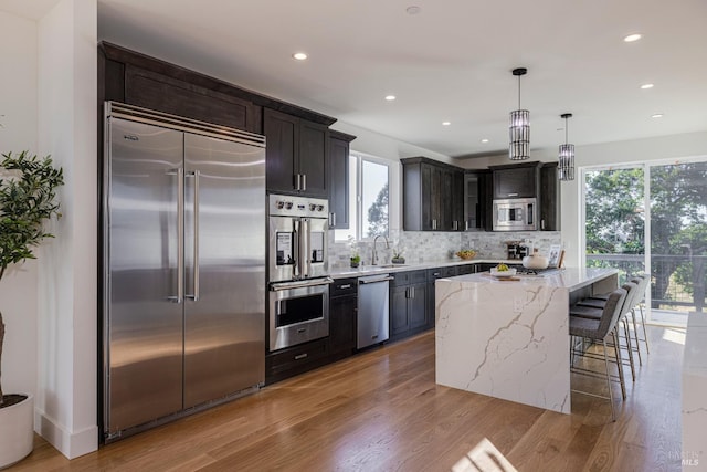 kitchen featuring sink, built in appliances, light stone countertops, a kitchen island, and decorative light fixtures