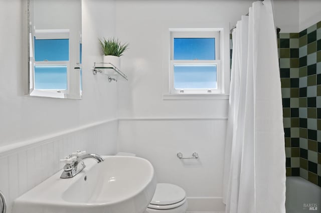 bathroom featuring a sink, a wainscoted wall, toilet, and shower / tub combo with curtain