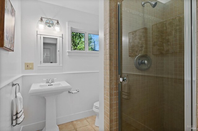 bathroom featuring toilet, a shower with shower door, and tile patterned flooring