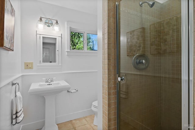 bathroom featuring tile patterned floors, toilet, a stall shower, a sink, and baseboards