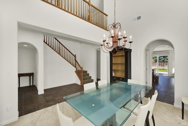 unfurnished dining area with a towering ceiling, dark tile patterned floors, and an inviting chandelier