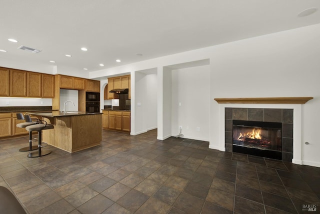 kitchen with a kitchen island with sink, a tiled fireplace, sink, black oven, and a breakfast bar area