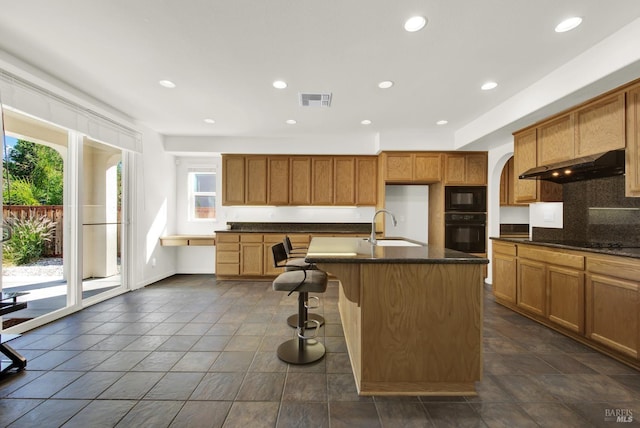 kitchen featuring black appliances, a wealth of natural light, an island with sink, and sink