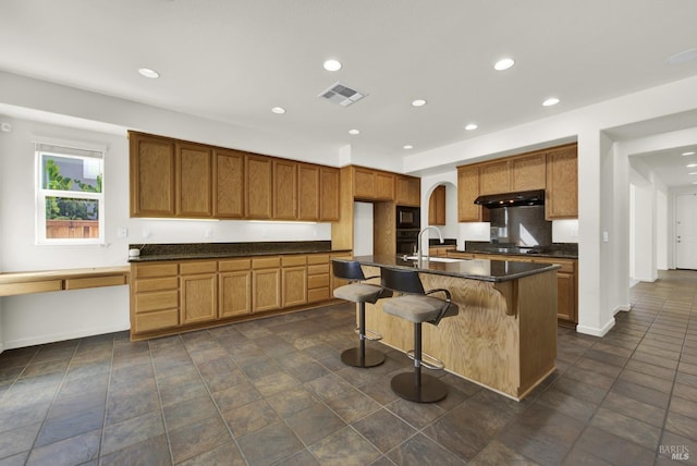 kitchen featuring black appliances, a kitchen bar, and an island with sink