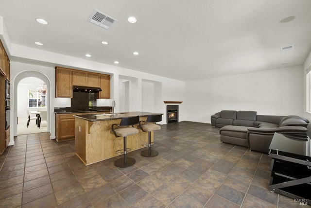 kitchen featuring backsplash, a kitchen bar, an island with sink, sink, and black oven