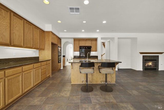 kitchen with a tiled fireplace, oven, sink, a kitchen breakfast bar, and a kitchen island with sink