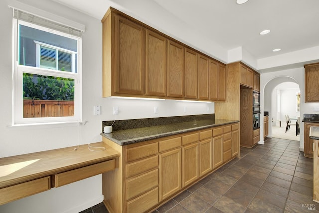 kitchen featuring stainless steel microwave, dark stone counters, and black oven