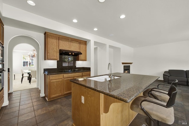 kitchen with a chandelier, sink, dark stone counters, a kitchen bar, and a kitchen island with sink