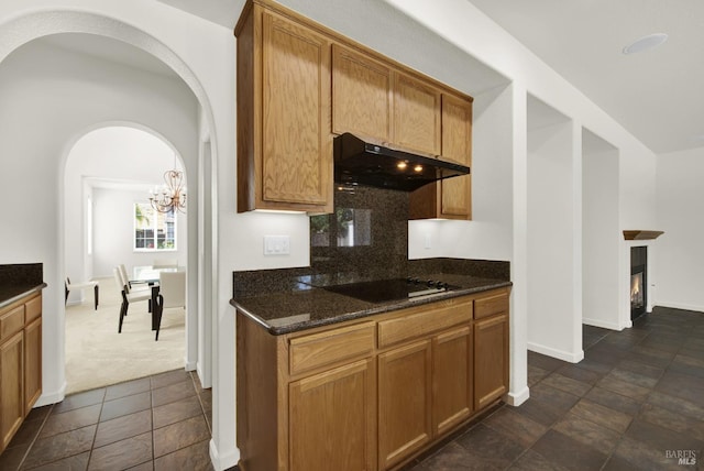 kitchen featuring backsplash, a notable chandelier, dark stone counters, dark carpet, and black electric stovetop