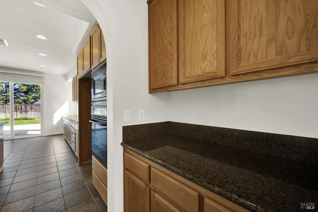 kitchen featuring oven, dark stone counters, dark tile patterned flooring, and built in microwave