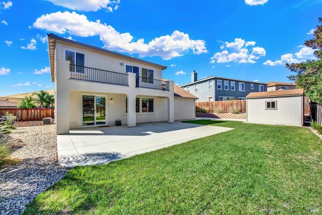 rear view of property with a balcony, a yard, a storage unit, and a patio area