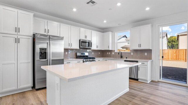 kitchen with a kitchen island, appliances with stainless steel finishes, sink, white cabinets, and light hardwood / wood-style flooring