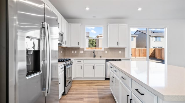 kitchen featuring sink, light hardwood / wood-style flooring, appliances with stainless steel finishes, white cabinets, and decorative backsplash