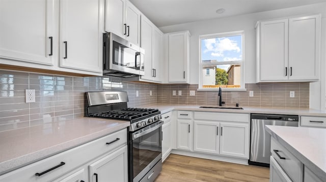 kitchen with stainless steel appliances, light hardwood / wood-style flooring, sink, white cabinets, and decorative backsplash