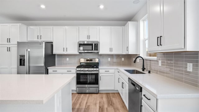 kitchen with appliances with stainless steel finishes, light wood-type flooring, white cabinets, decorative backsplash, and sink