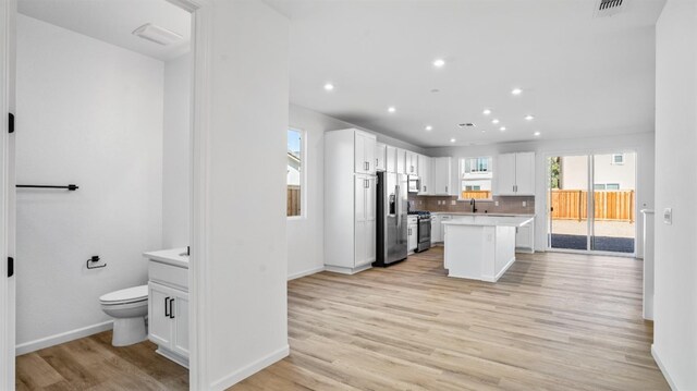 kitchen with light wood-type flooring, a kitchen island, white cabinets, stainless steel appliances, and backsplash