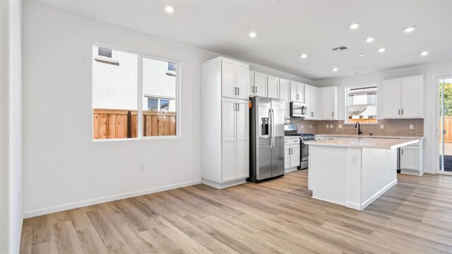 kitchen featuring tasteful backsplash, white cabinets, a center island, stainless steel appliances, and light wood-type flooring