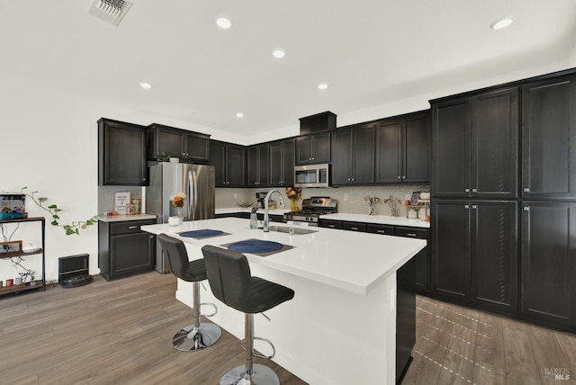 kitchen with appliances with stainless steel finishes, sink, wood-type flooring, a kitchen bar, and a center island with sink