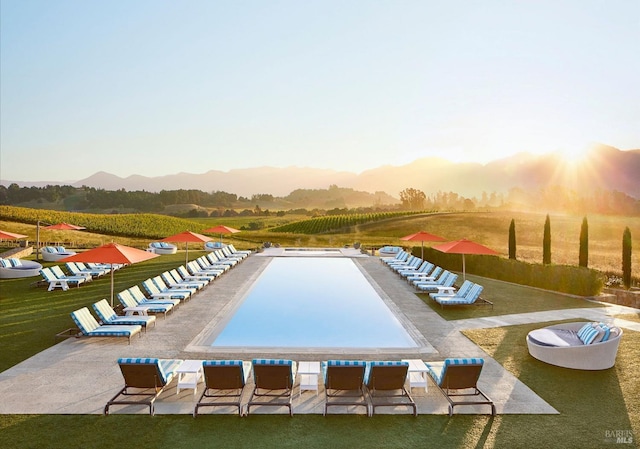 pool at dusk with a patio area and a lawn