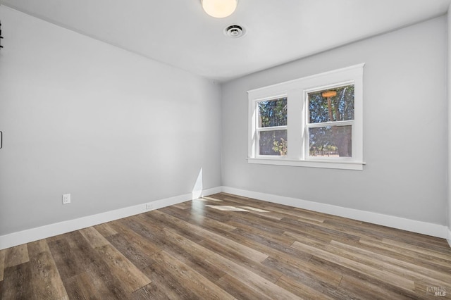 empty room with baseboards, visible vents, and wood finished floors